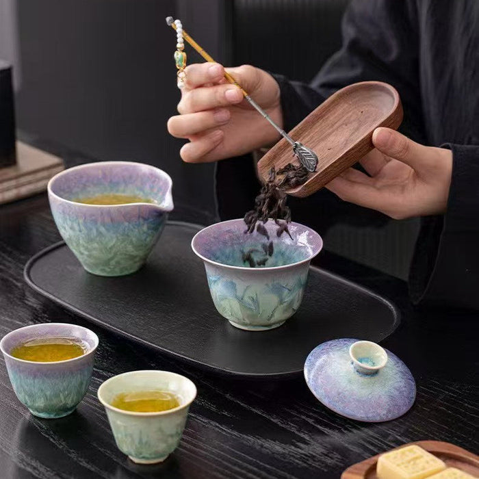 Person performing a tea ceremony with ceramic cups and a tray on a dark surface.