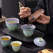 Person performing a tea ceremony with ceramic cups and a tray on a dark surface.